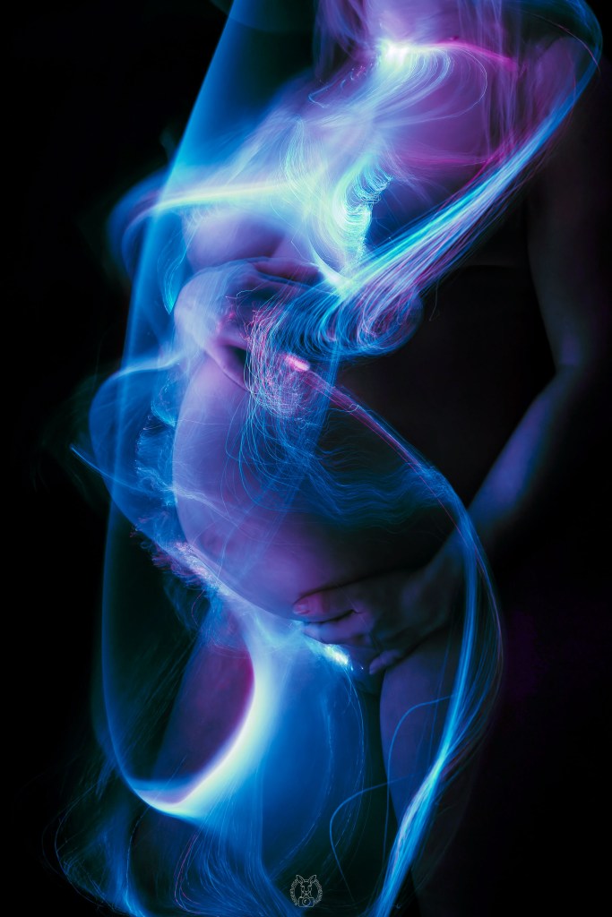 Künstlerische Darstellung einer schwangeren Frau mit leuchtenden blauen und violetten Lichtspuren, die sich um ihren Körper ziehen. Die Szene wirkt verträumt und futuristisch.